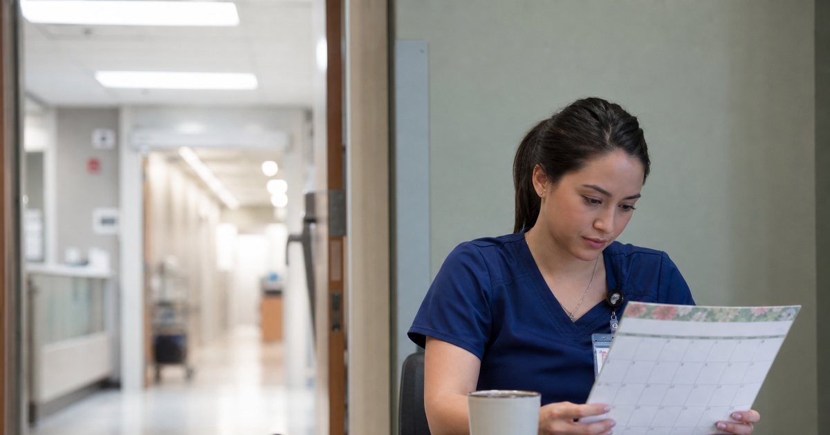 A nurse in scrubs sitting alone at a break room table with a coffee cup, looking thoughtfully toward the window, a hospital corridor visible through the doorway